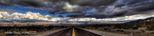 Pnorama of a lonely road through Mojave Desert under a dramatic sky.