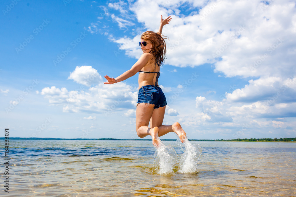 Naklejka premium Beautiful young sexy model in the sea. Lovely young woman jumping on the sunny beach