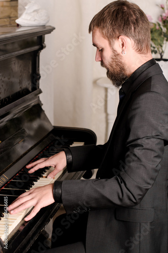 Молодой мужчина с бородой и в костюме играет на пианино 