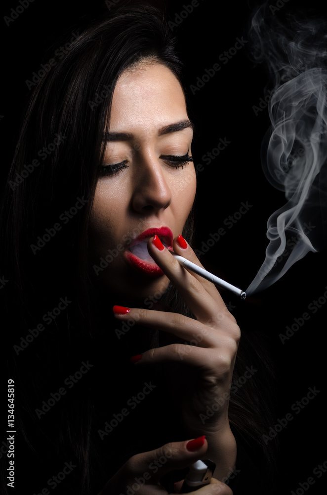 Fototapeta premium Portrait of the beautiful elegant girl smoking cigarette on black background.