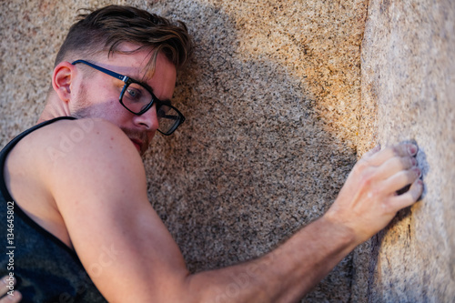 Young caucasian man wearing glasses climbs a granite cliff in the desert photo