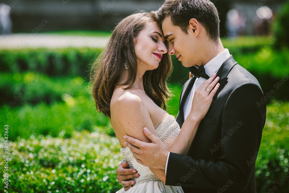 Naklejka premium Bride and groom lean to each other tender standing among green b