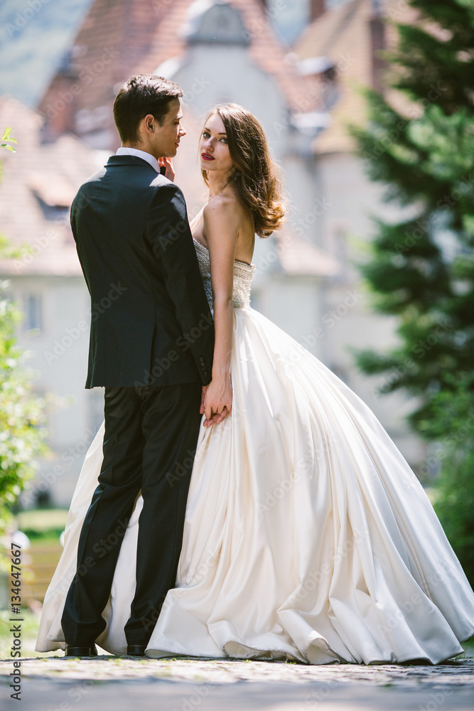 Bride in luxurious ivory dress looks over groom's shoulder while