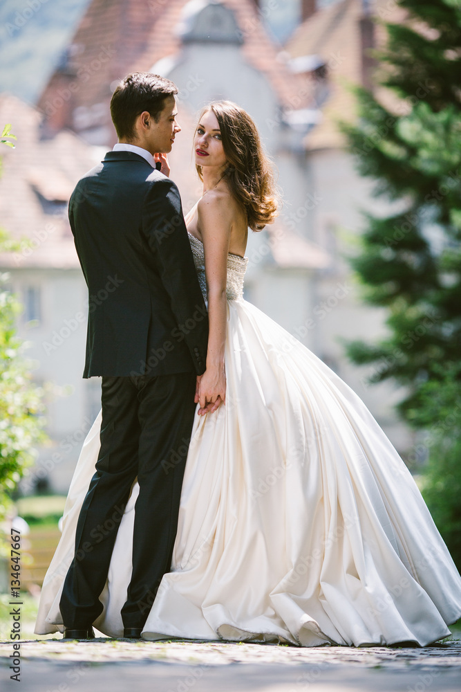 Naklejka premium Bride in luxurious ivory dress looks over groom's shoulder while