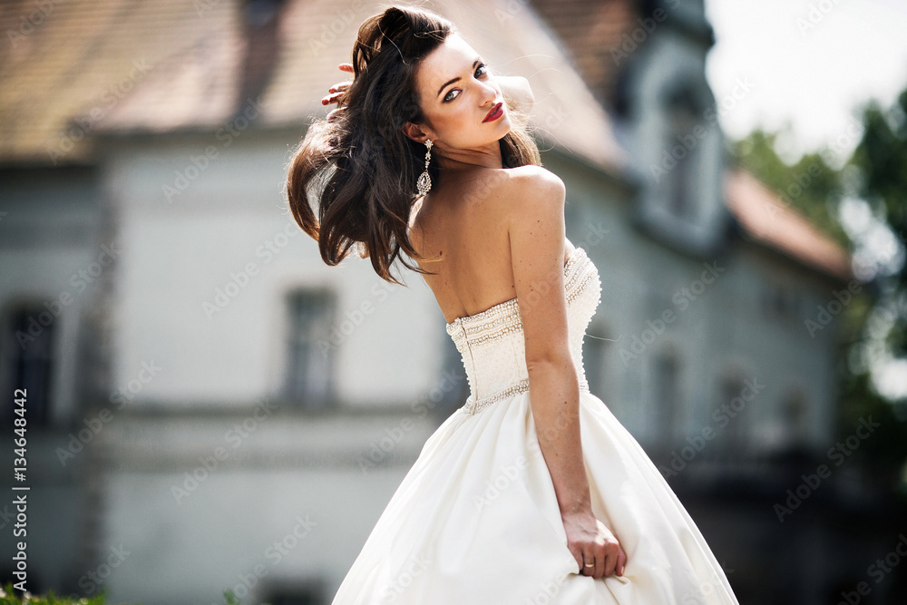 Naklejka premium Bride touches her silky brown hair while she poses in ivory dres