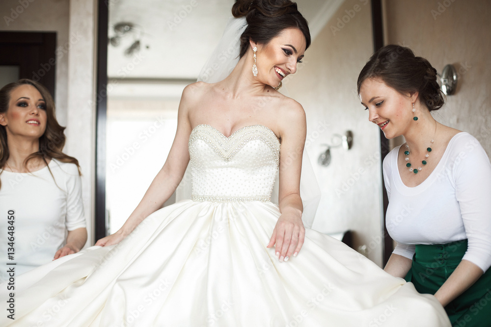 Bride looks over her shoulder and smiles while bridesmaids fix h
