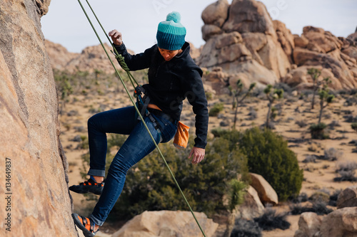 Young african american woman climbs along a granite cliff in the desert dressed for cold weather photo