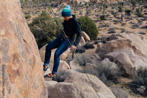 Young african american woman climbs along a granite cliff in the desert dressed for cold weather
