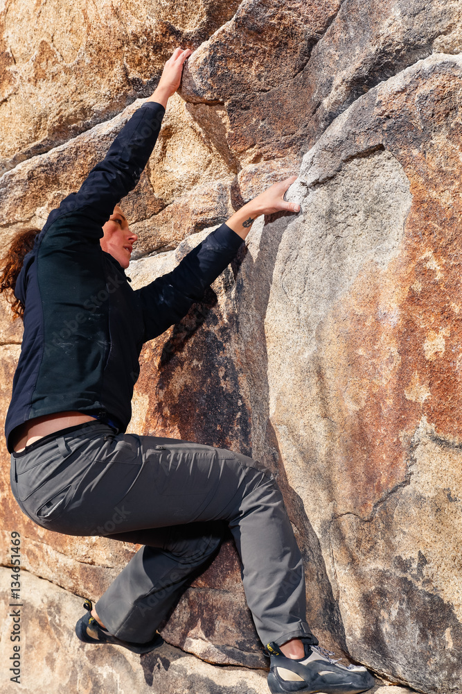 Young caucasian woman climbs along a granite cliff in the desert