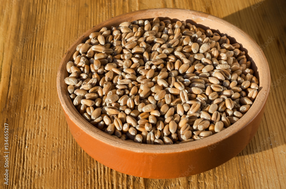 Grains of wheat in a clay bowl on a wooden background texture. Selective focus. Grains of wheat in a clay bowl on a wooden background texture. Selective focus.