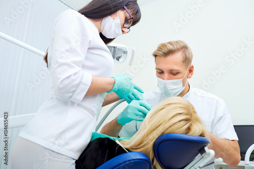 Dentist man with assistant treats teeth patient in hospital office