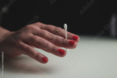 Hand with red nails holding the cotton bud