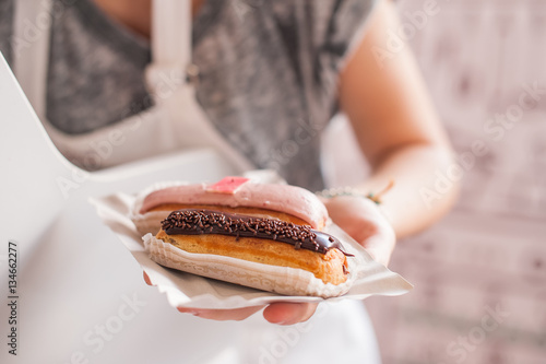 Female saller holding eclairs to the bayer at market. Soft selective focus, close up photo