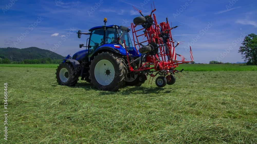 A big blue tractor is standing in the middle of the grass field and agricultural machinery is being connected to it.
A big blue tractor is standing in the middle of the grass field and agricultural machinery is being connected to it.