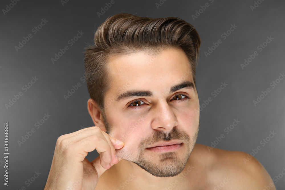 Obraz premium Young handsome man examining his face on grey background
