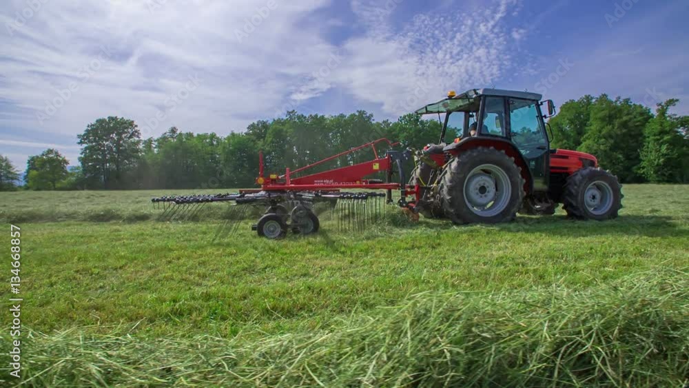 A farmer is driving a tractor on a large field and he is organizing hay in different lines.
A farmer is driving a tractor on a large field and he is organizing hay in different lines.