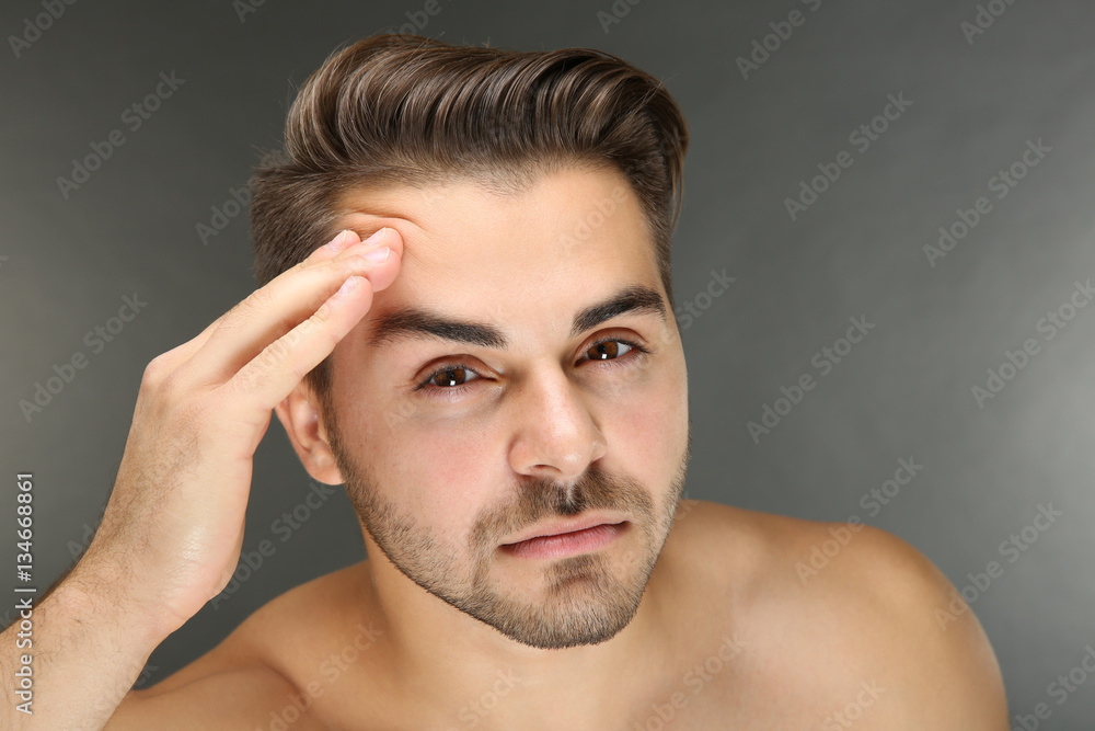 Young handsome man examining his face on grey background Young handsome man examining his face on grey background