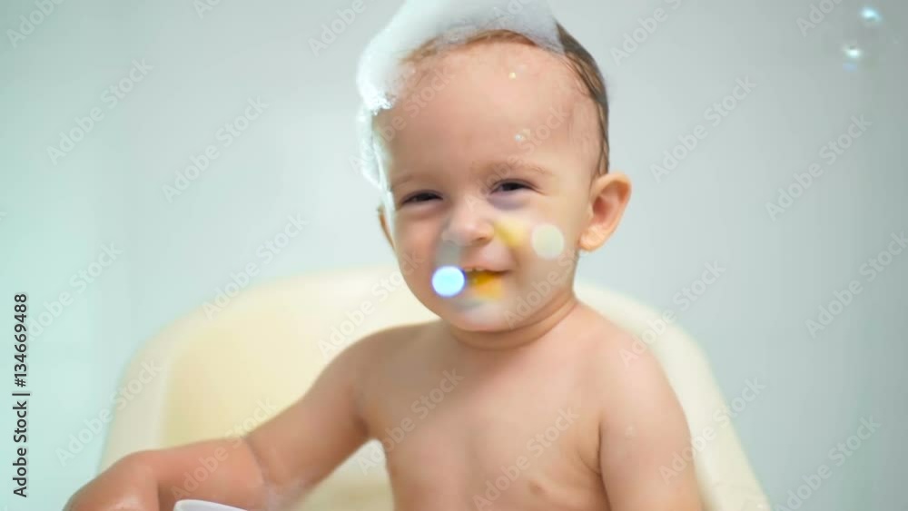 Slow motion video of happy laughing baby boy bathing and looking at flying soap bubbles Slow motion video of happy laughing baby boy bathing and looking at flying soap bubbles