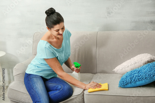 Young woman cleaning sofa w...