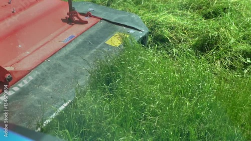 A young farmer is cutting grass on a field with a grass cu. tting machine. The day is sunny and it is warm outside.
 photo