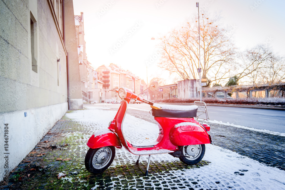 Red retro motorcycle scooter parked along a street covered with snow in the winter in the city of Bern, Switzerland.