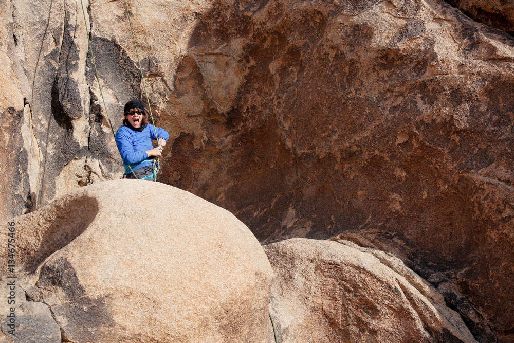 Naklejka premium Young caucasian woman dressed for cold weather rock climbing in the desert climbs a cliff. Wearing a jacket, hat, and glasses
