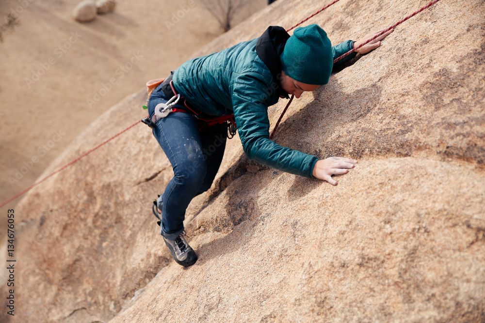 Young caucasian woman dressed for cold weather rock climbing in the desert climbs a cliff Young caucasian woman dressed for cold weather rock climbing in the desert climbs a cliff