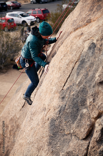 Young caucasian woman dressed for cold weather rock climbing in the desert climbs a cliff