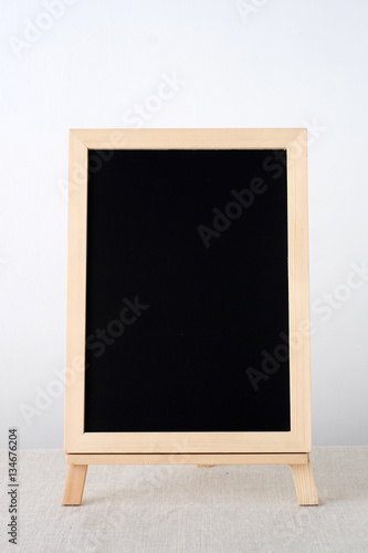 Blank chalkboard standing on sack tablecloth over white cement wall background