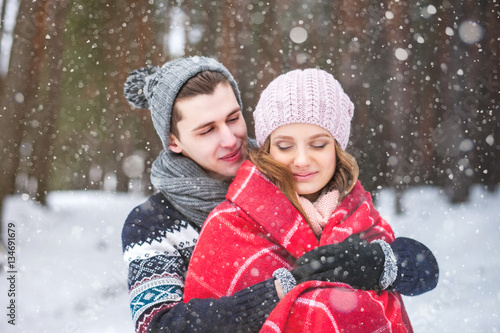 The guy embraces the girl and covers it with a warm blanket in the winter forest, couple of lovers