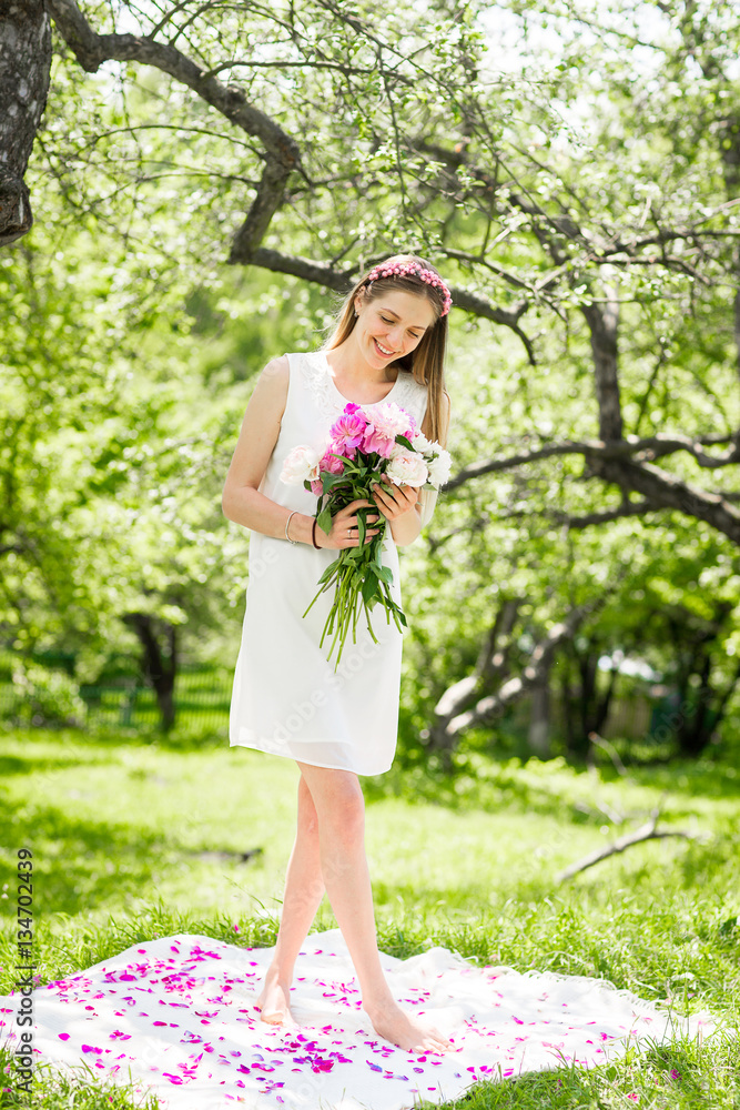 Gentle happy brunette woman with bouquet of peonies in among the trees a sunny day Gentle happy brunette woman with bouquet of peonies in among the trees a sunny day