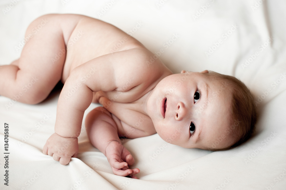 Soft picture of a beautiful baby boy laying on white bedding Soft picture of a beautiful baby boy laying on white bedding