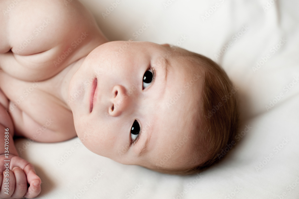 Soft picture of a beautiful baby boy laying on white bedding Soft picture of a beautiful baby boy laying on white bedding