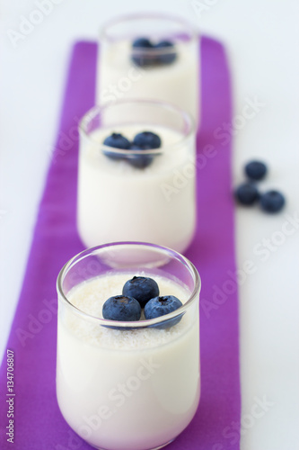 Three small cups of the coconut panna cotta with blueberries on a purple napkin. White background, selective focus
