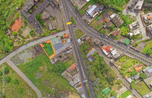 An overhead aerial view of a small town with a winding road through residential houses and green trees near Banos, Ecuador, a peaceful community from above.