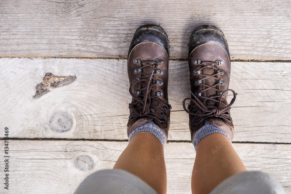 Downward view of heavy hiking boots. Female hiker standing on a wooden platform.