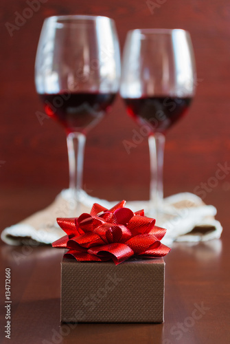 Two glasses of wine on a wooden table. Brown box with a bow.