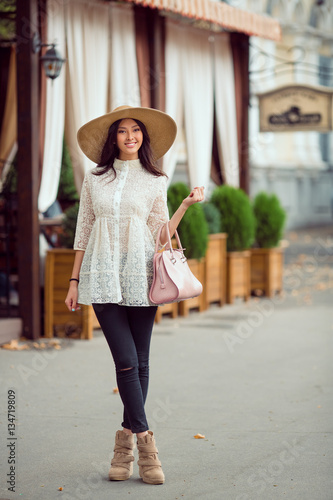 Stylish young asian girl walking on city street against cafe facade