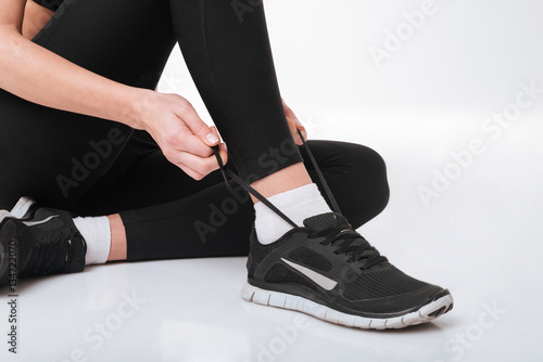 Closeup of sportswoman sitting and tying shoelaces