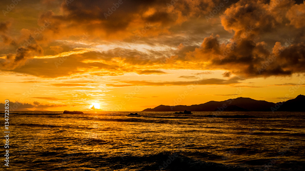 Amazing orange and cloudy sunset in a tropical island, Anse Severe beach, La Digue, Seychelles