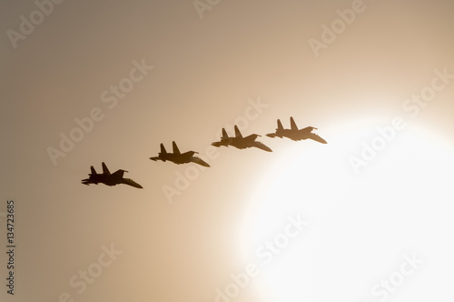 4 Su-27 Flanker jet fighters fly in back lit against cloudy sky background
 photo