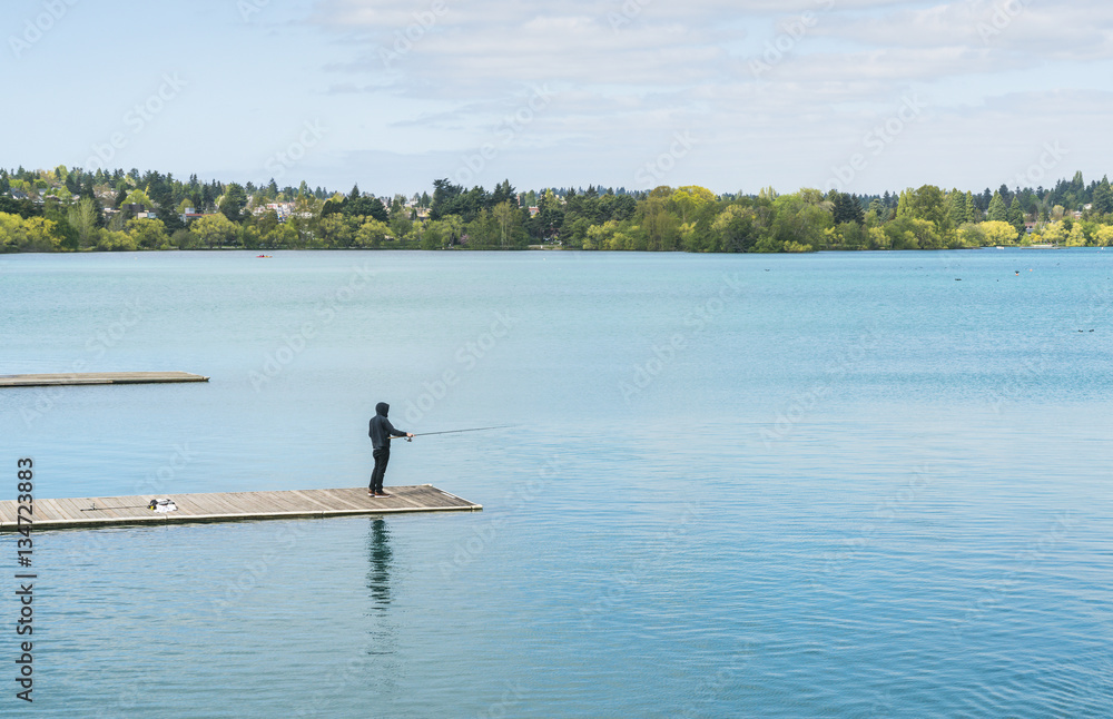 a man fihing in the blue lake  in the  park.