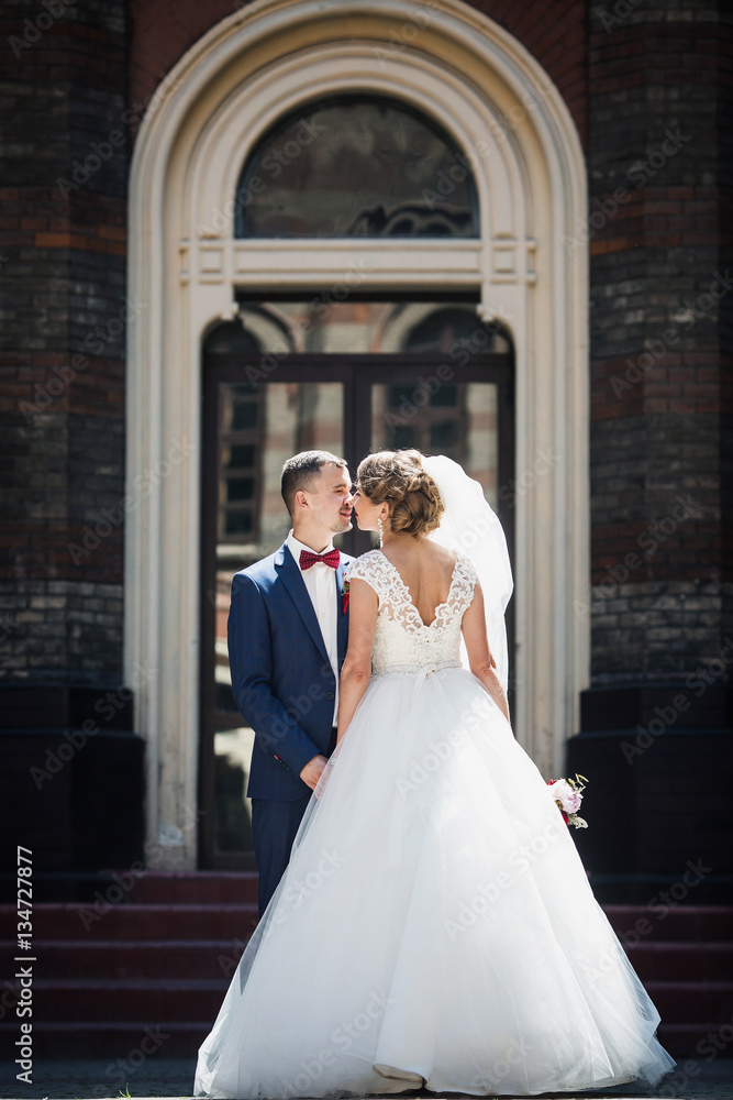 Shiny newlyweds kiss before the tall entrance to an old house