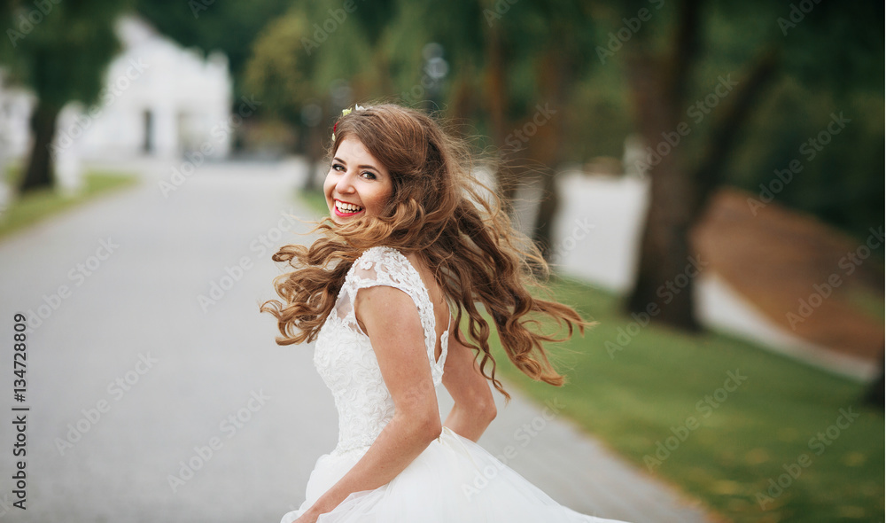 Cheerful bride with long dark blonde hair whirls on path in park Cheerful bride with long dark blonde hair whirls on path in park
