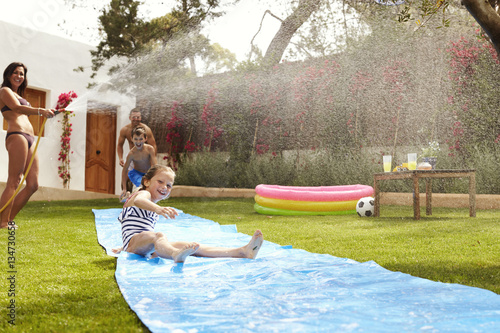 Family Having Fun On Water Slide In Garden photo