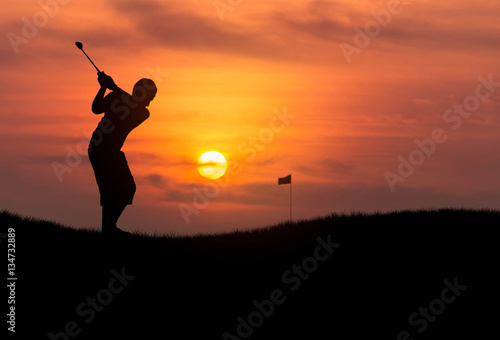 silhouette the boy golfer hit golf ball toward the hole at sunset