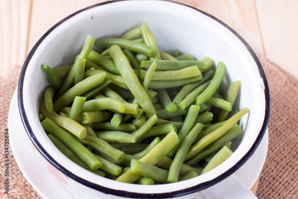Colander with leguminous of green raw beans on the cutting board on the kitchen table Colander with leguminous of green raw beans on the cutting board on the kitchen table