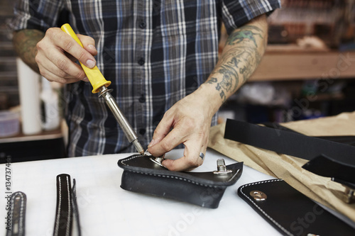 A leather worker and craftsman using a hand held tool on a blue leather bag on a workbench  photo