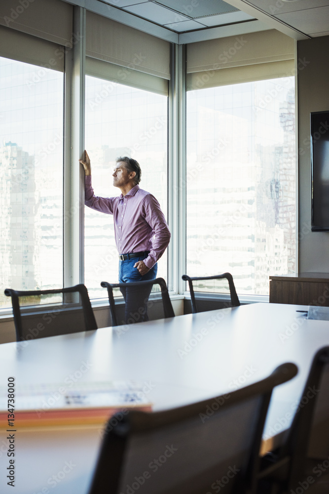 A man in a meeting room looking out of a window at an urban landscape.