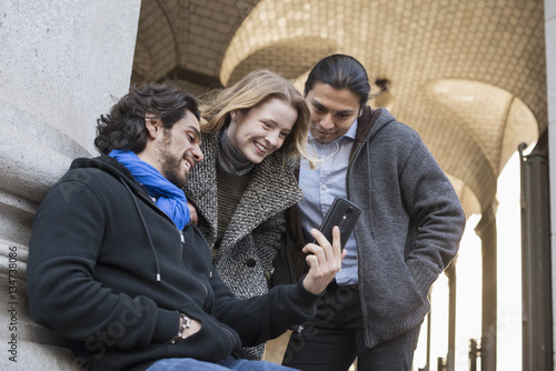 Three people, two men and a woman looking at the screen of a smart phone. 